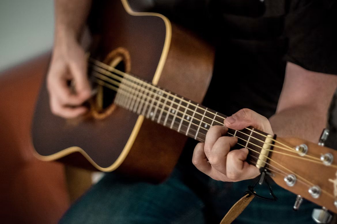 Close-up of a person playing an acoustic guitar, one hand fretting chords on the neck, the other strumming the strings